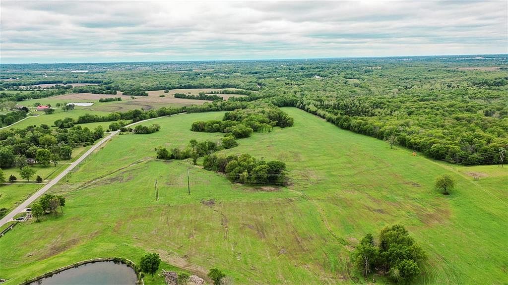 A wide aerial of 80 acres of rolling pasture and timber south of Longview Lake, with Kansas City reading faintly on the northern horizon